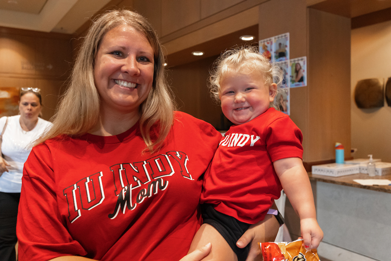 A woman wearing a shirt that says "IU Indy mom" holding a baby wearing a shirt that says "IU Indy".